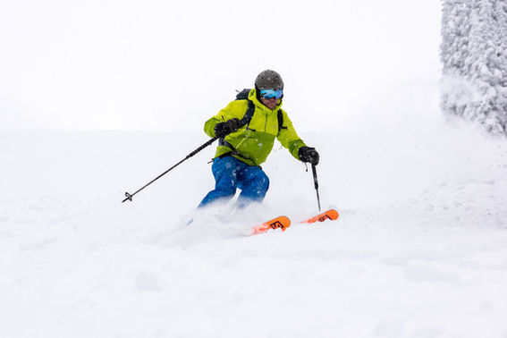 Man wearing a green ski jacket and blue ski pants, skiing in powder snow