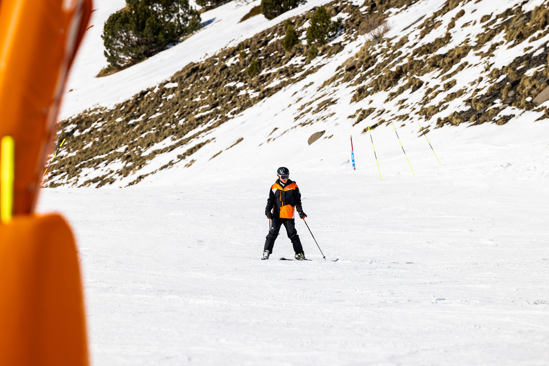 A male skier wearing a black and orange ski suit skiing down a slope.