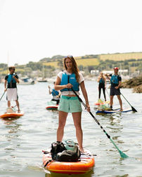 Woman standing on a paddle board paddling down a river in front of a group of people