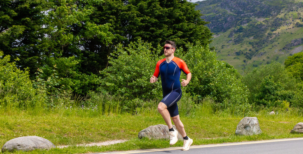 A man wearing a red and navy blue triathlon suit running along a road. 