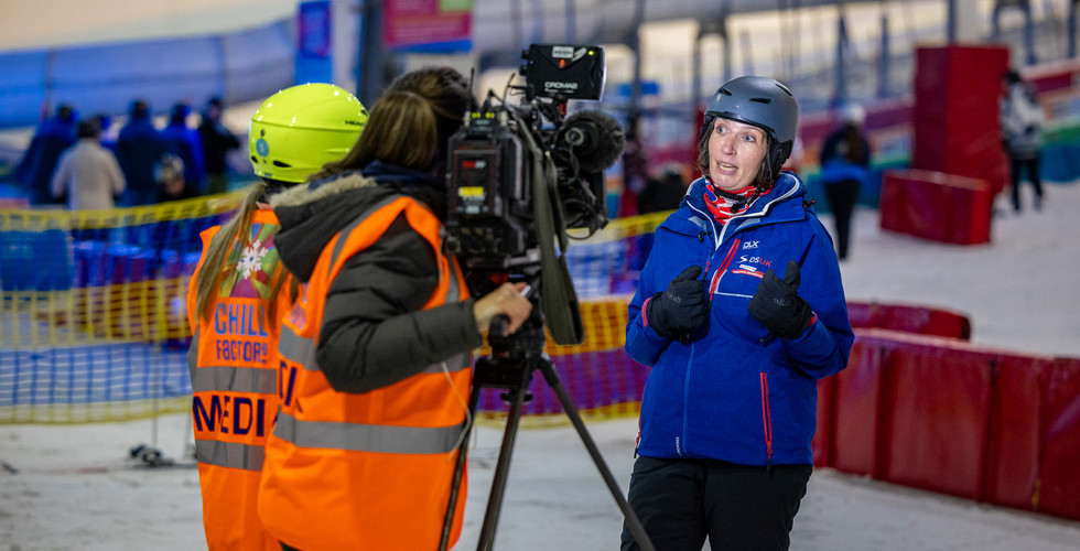 Woman in a blue ski jacket being interviewed by a TV crew