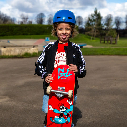 A young boy wearing a helmet and holding a skateboard sticking his tongue out.