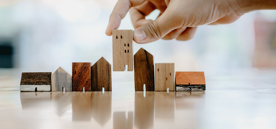 Hand choosing mini wood house model from model and row of coin money on wood table, select