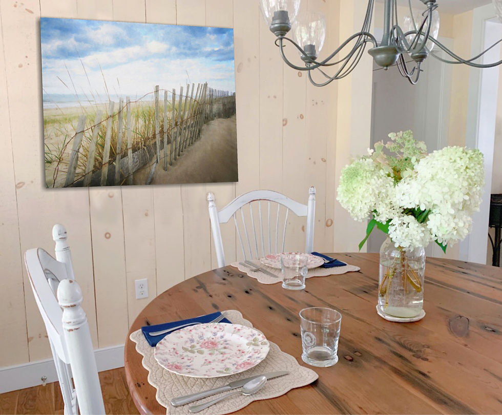 Dining table set with floral plates, blue napkins, and glassware. Vase of white flowers on table. Beach fence, sand and sea grass wall art
on wood-paneled wall. Cozy feel.