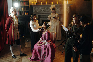 Équipe de tournage cinéma avec maquilleuse réalisant une retouche sur une actrice en costume d’époque.