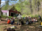 A group of students are seated in a circle outdoors in front of a large barn.