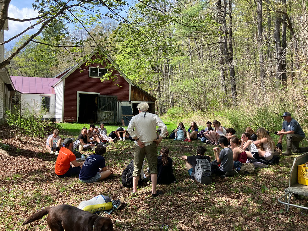 A group of students are seated in a circle outdoors in front of a large barn.