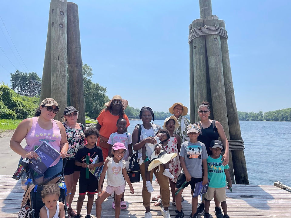 Group of people including young children posing together and smiling on a pier in front of the Connecticut River