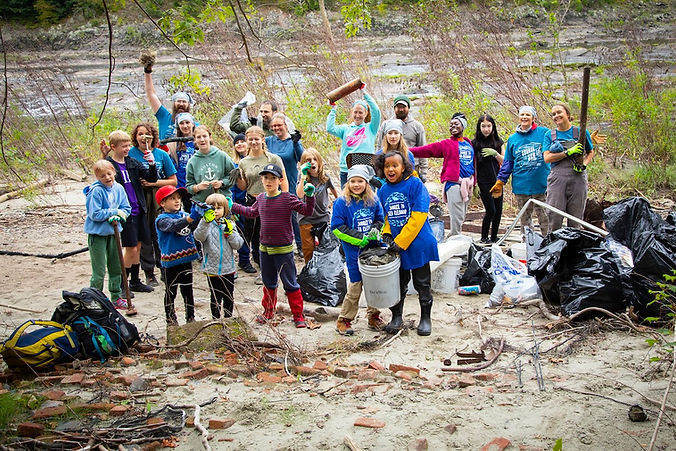 Group of happy kids with trash cleanup supplies outdoors. Source to Sea Cleanup - Deer Paths Nature School by Beth Pelton.