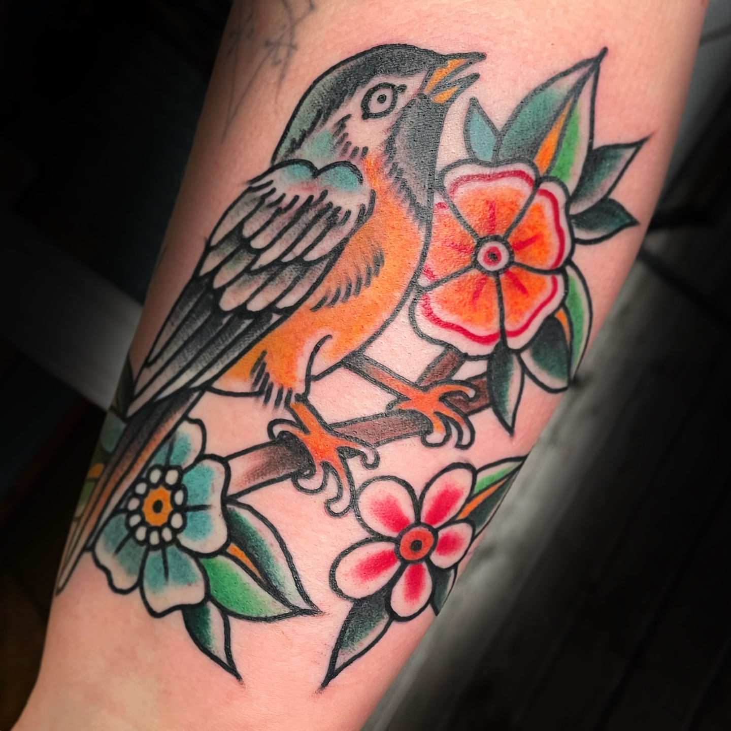a tattoo of a bird sitting on a branch with flowers