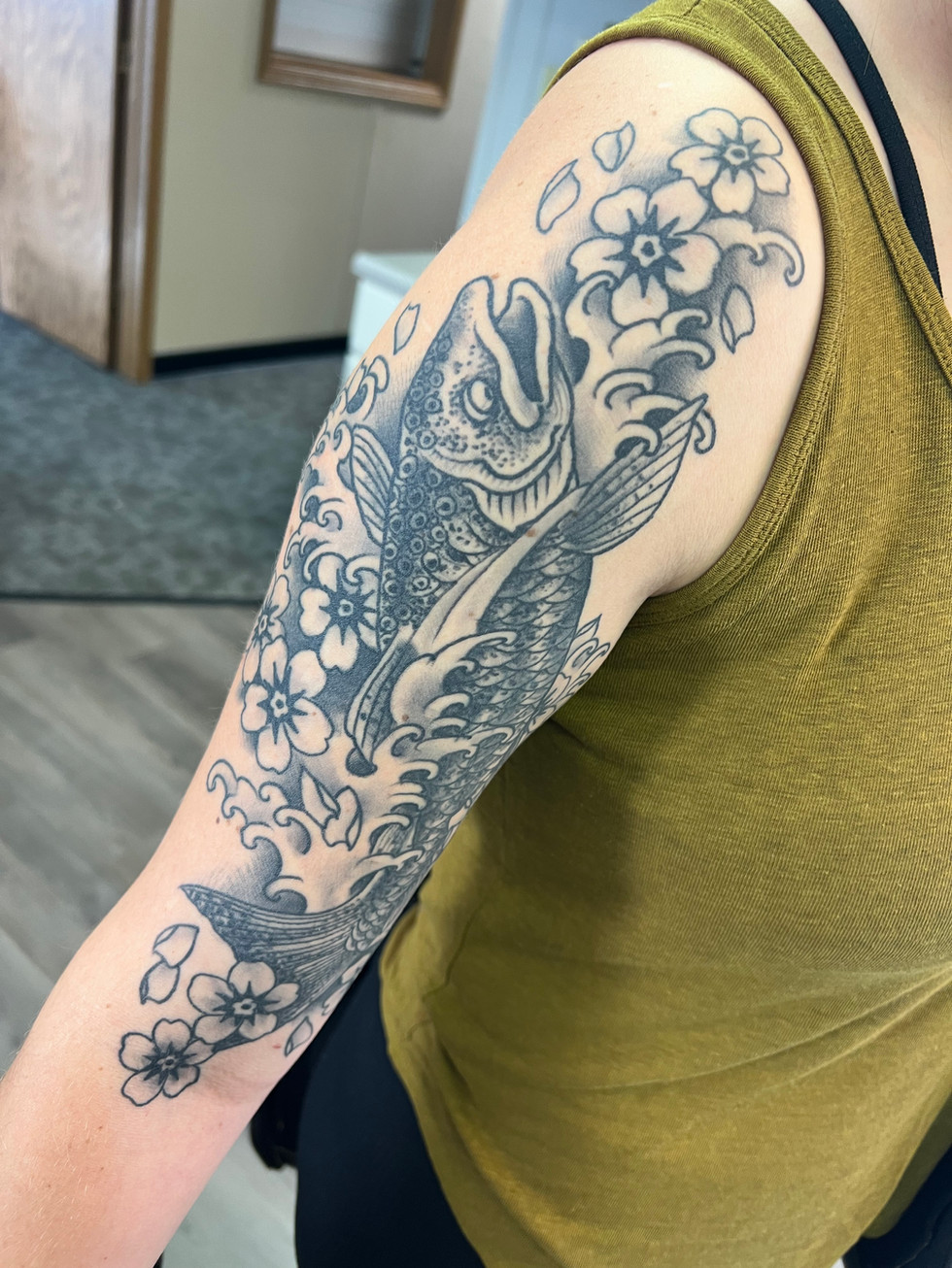 a woman has a tattoo of a fish and flowers on her arm