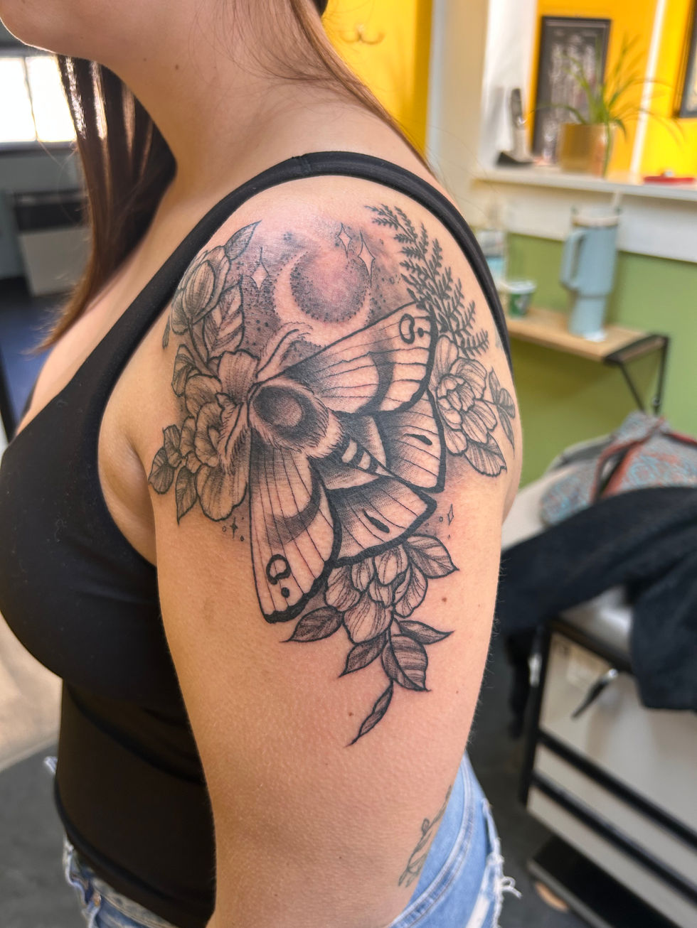 a woman has a tattoo of a moth and flowers on her shoulder