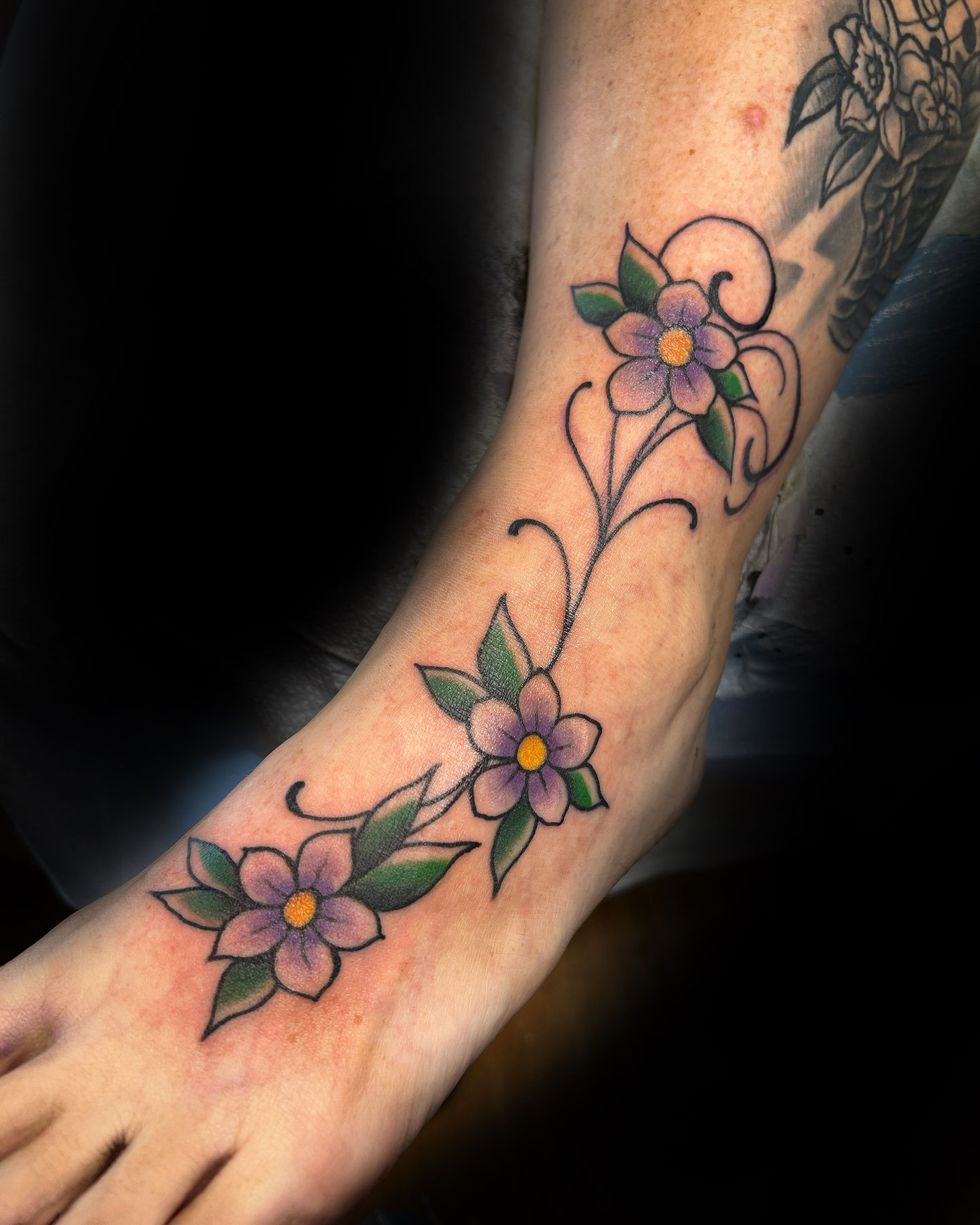 a person has a tattoo of purple flowers on their foot