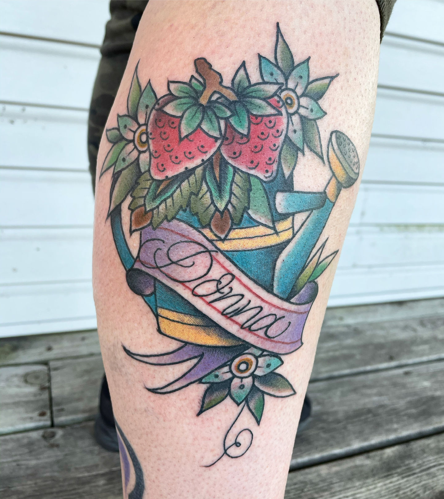 a tattoo of a watering can with strawberries and the name donna