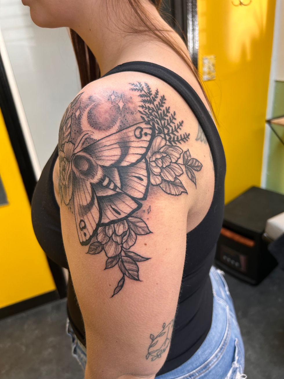 a woman has a tattoo of a moth and flowers on her shoulder