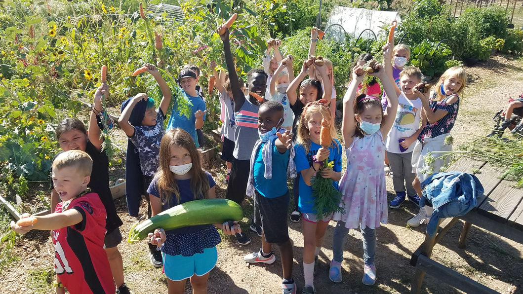 Children holding up veggies they grew and cheering