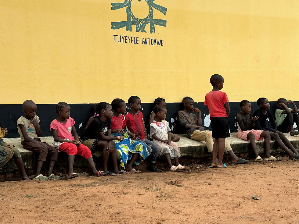 A group of children sitting along the walls of the youth corner and watching a celebratory performance