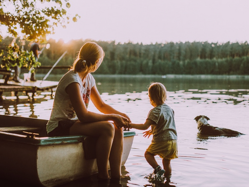 Image of woman and young child in and around a boat on a lake with a dog swimming nearby.