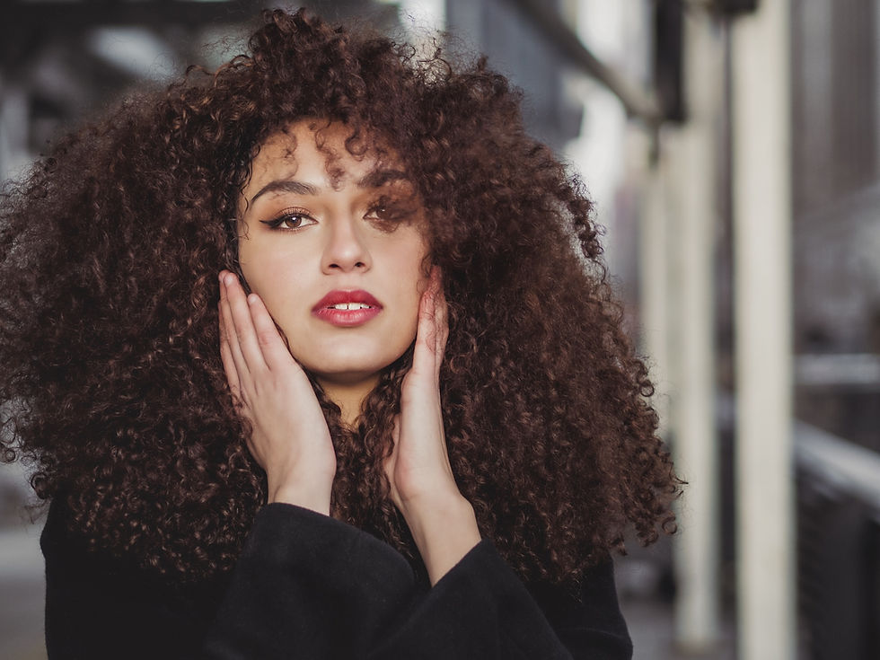 Portrait of a young woman with voluminous curly hair holding her face with both hands, captured by a people photographer.