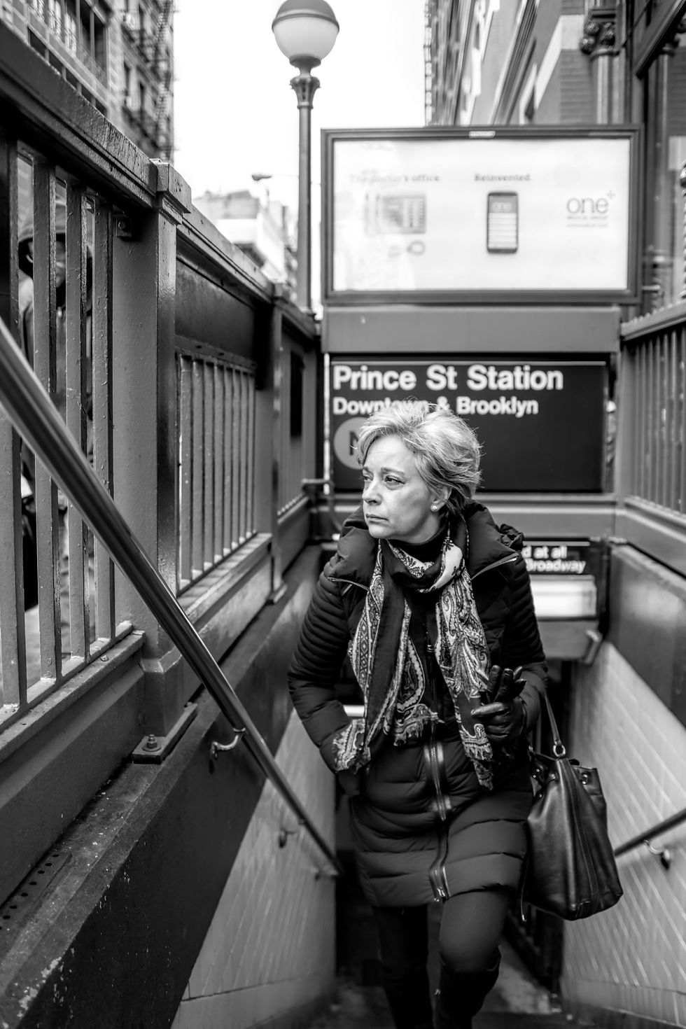 A person climbing subway stairs between metal railings beneath a Prince St Station sign, in black and white.