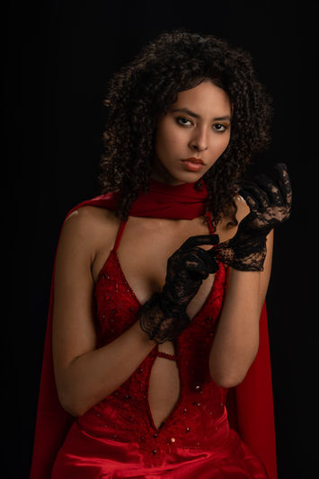 ChatGPT said:
Studio portrait of a woman in a red dress adjusting lace gloves against a dark background.