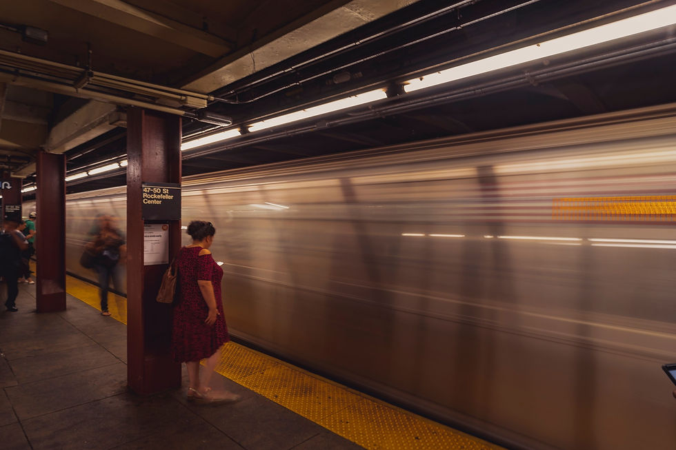 A person standing near a subway column and yellow platform edge beside a motion-blurred train.