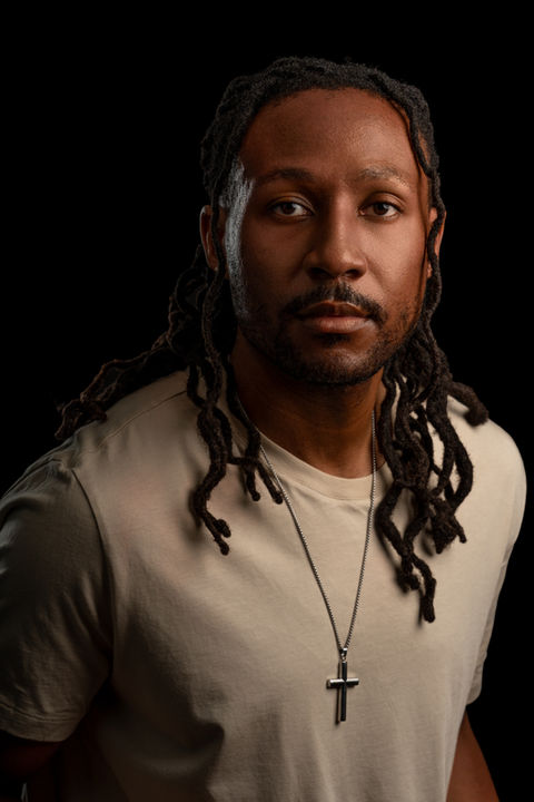Cinematic portrait of a man with locs wearing a cross necklace, photographed in studio with dramatic lighting by Rahway, NJ portrait photographer Ramon Trotman.