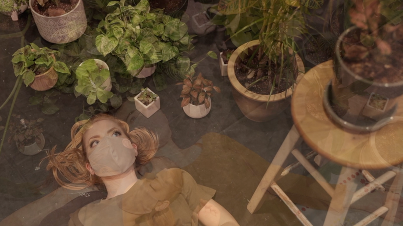 A woman lays on the floor, surrounded by plants. The image is slightly overlaid with another images of a different women in a similar position.