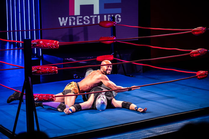 Two men at the center of a wrestling ring, the one on top pinning the one underneath.