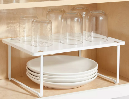 White metal shelf riser organizing plates below and glass cups above to maximize vertical cabinet storage space in Dallas Texas kitchen