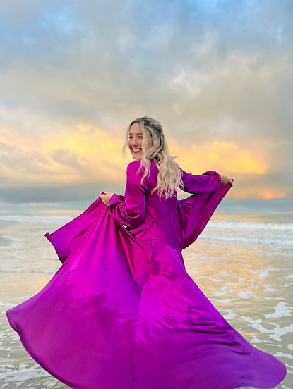 Sarah Sanders smiling in a purple dress while standing in the ocean at sunset, photo by Sarah Sanders Creative