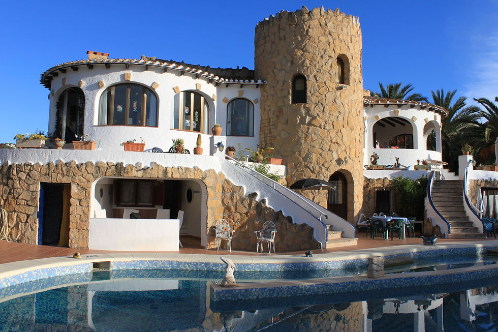 Villa méditerranéenne en pierre et blanc avec tour, piscine bleue au premier plan et ciel clair en arriÚre-plan.