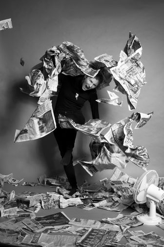 Eine schwarzweiß Fotografie von einer Frau die brüllend sich von Zeitungen befreit.