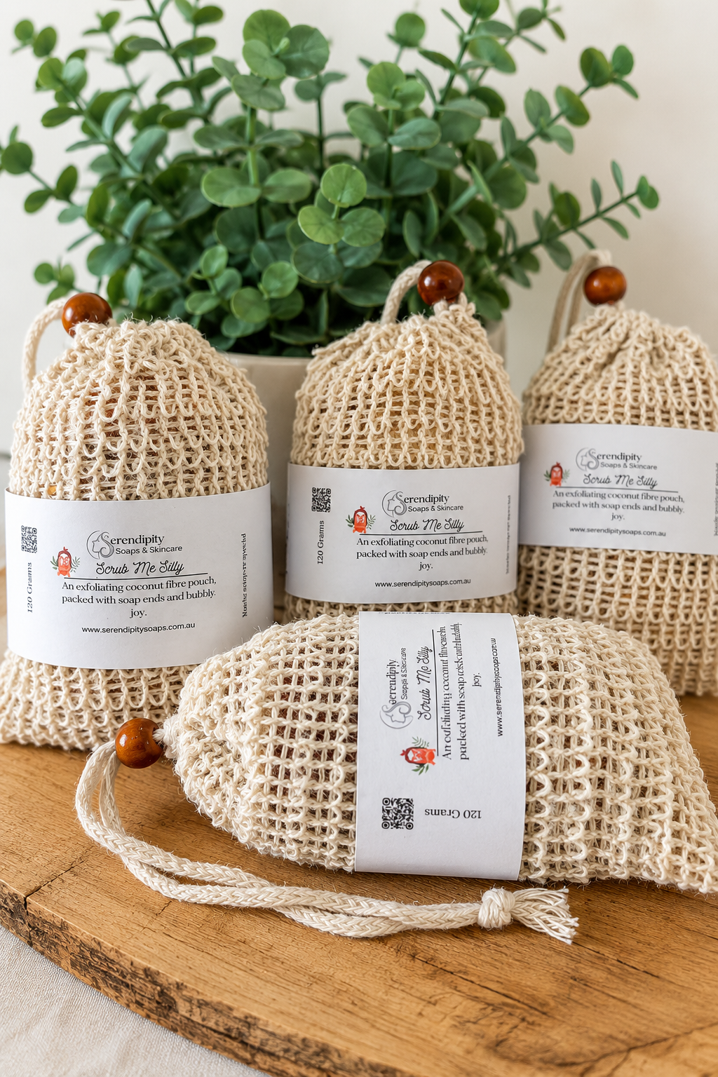 Natural eco fibre soap saver pouches filled with handmade soap off cuts displayed on a wooden table with greenery in the back