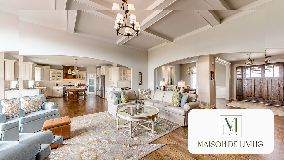 Spacious living room with beige L-shaped sofa, colorful cushions, wooden floor, large windows, and rustic door. "Maison De Living" logo.