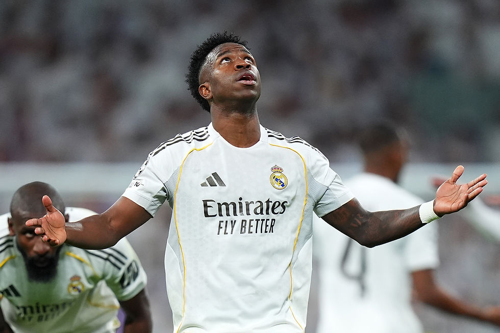 Soccer player in a white Real Madrid jersey looks upward with arms outstretched. Another player is visible in the background.