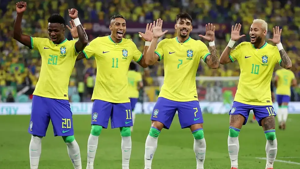 Four Brazil soccer players in yellow jerseys celebrate with raised hands on the field, with a blurred cheering crowd behind.