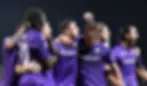 Soccer team in purple jerseys celebrates, arms around each other, with one player raising a fist. "Mediacom" visible on shirts, joyous mood.
