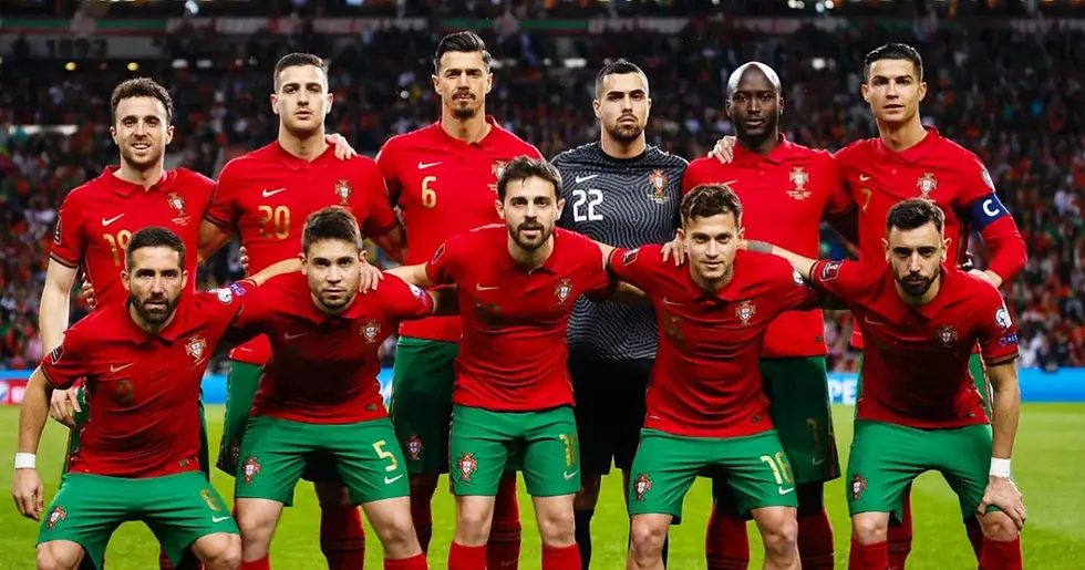 Portugal men’s soccer team poses for a pre-match photo in red jerseys and green shorts, stadium crowd blurred behind.