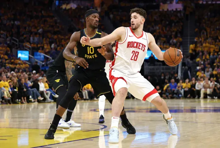 Basketball game scene: Player in white Rockets jersey dribbles while guarded by player in black State jersey. Crowd in yellow in the background.