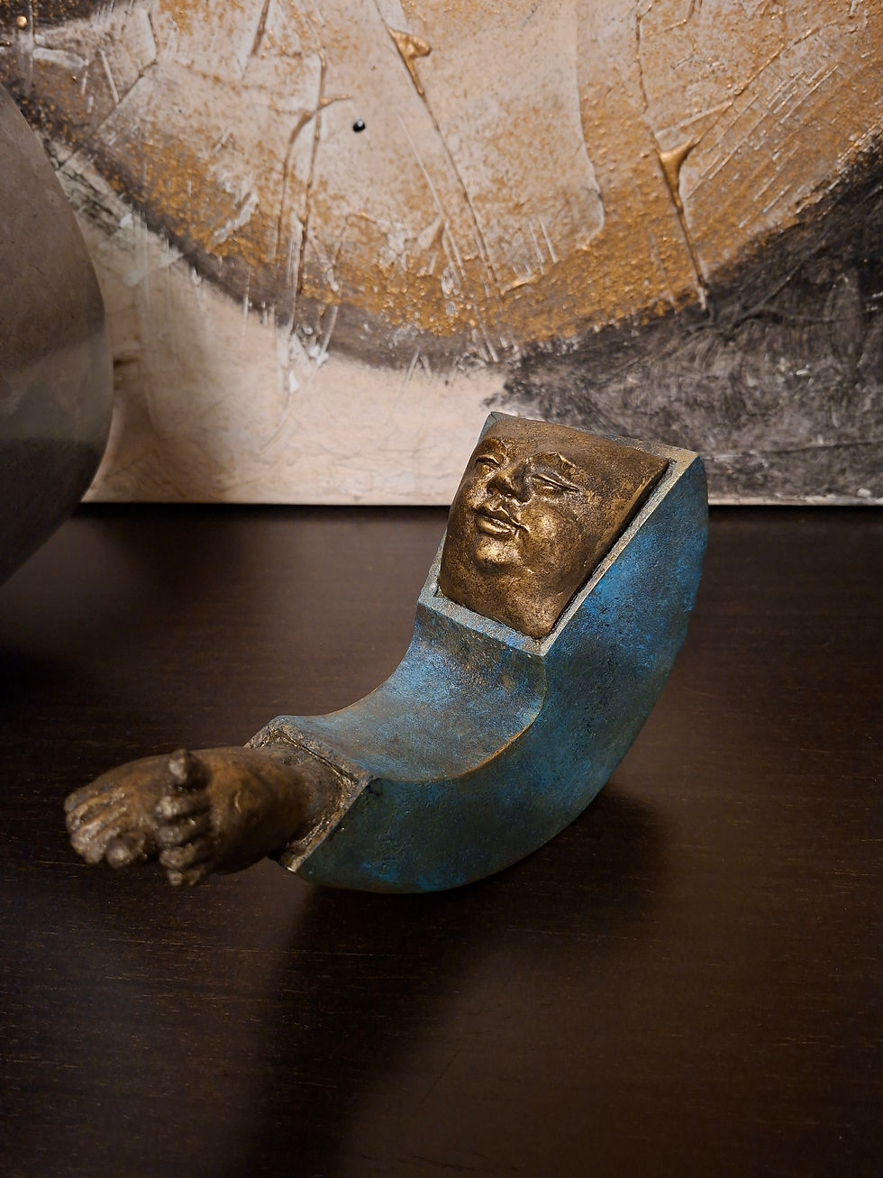 Miniaturbild: Pequena escultura metálica curvada azul com rosto e mão dourados.