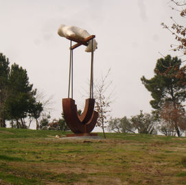Escultura gigante de alfinete de segurança em colina gramada, sob céu nublado.