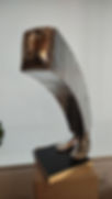 Escultura de bronze de pessoa curvada sobre livro aberto, arte moderna.