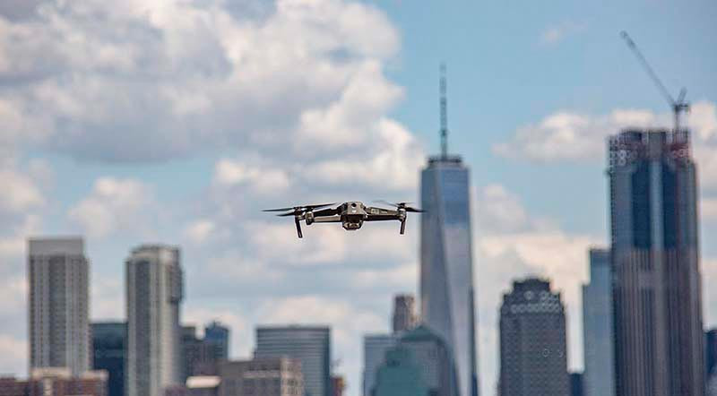 Drone flies over a city skyline of tall skyscrapers beneath a cloudy blue sky.