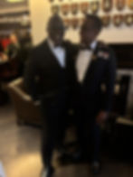 Two men in tuxedos smiling at a formal event with plaques.