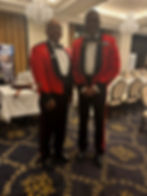 Two men in red military mess dress at a formal dinner.