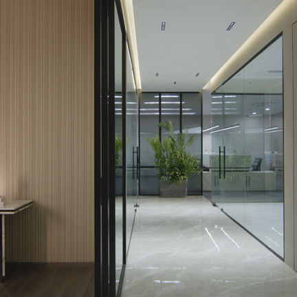 A minimalist luxury office hallway featuring sleek wood-paneled walls, bright recessed corridor lighting, and a glass-enclosed meeting room showing indoor plants