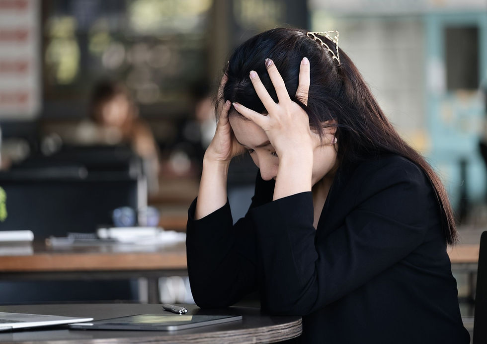 Autistic adult woman in a black blazer sits at a desk with her head in her hands, showing signs of mental exhaustion, stress, or autistic burnout.