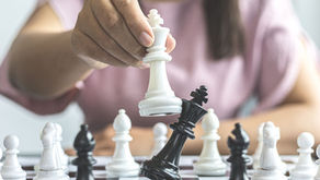 An autistic adult plays chess with deep focus, holding a white king piece after a strategic move. Image represents intense interest and concentration in autism.