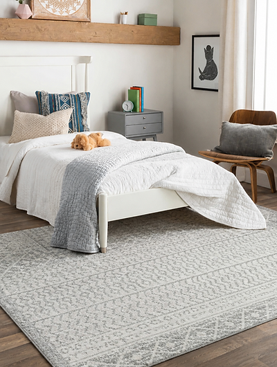 Gray patterned area rug styled beneath a white bed in a bright modern bedroom.